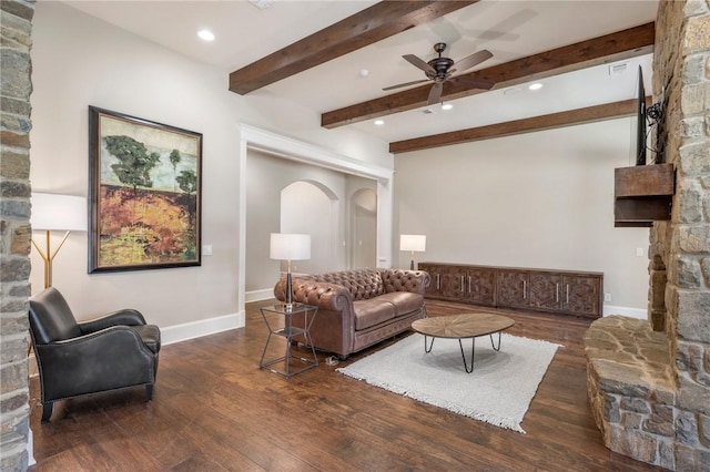 living room featuring arched walkways, a stone fireplace, wood finished floors, and beam ceiling