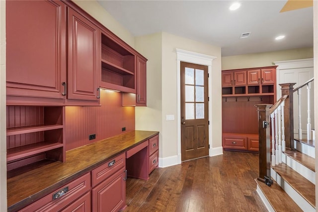 interior space with visible vents, open shelves, built in desk, dark countertops, and dark wood finished floors