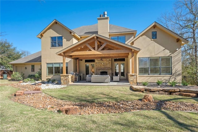 rear view of property featuring a patio, a chimney, stucco siding, a lawn, and an outdoor living space with a fireplace