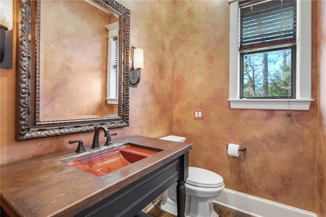 half bathroom with toilet, baseboards, and vanity