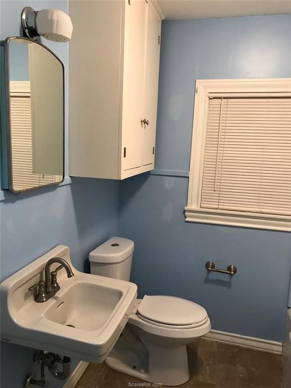 half bath featuring toilet, baseboards, and a sink