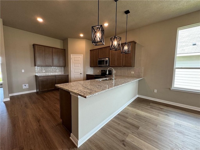 kitchen with dark hardwood / wood-style floors, decorative backsplash, light stone countertops, appliances with stainless steel finishes, and decorative light fixtures