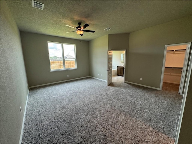 unfurnished bedroom with light carpet, a walk in closet, ceiling fan, a textured ceiling, and a closet