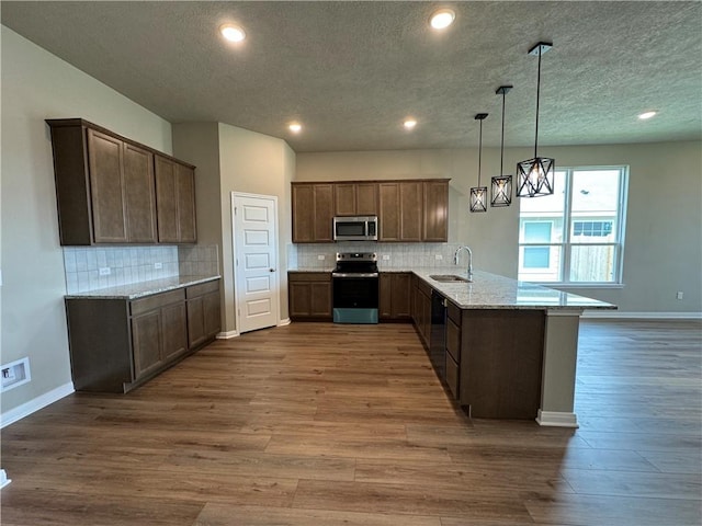 kitchen with sink, stainless steel appliances, kitchen peninsula, hardwood / wood-style floors, and pendant lighting