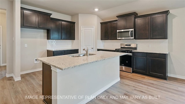 kitchen with stainless steel appliances, decorative backsplash, a kitchen island with sink, light stone counters, and sink