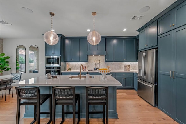 kitchen with appliances with stainless steel finishes, light wood-type flooring, pendant lighting, and an island with sink