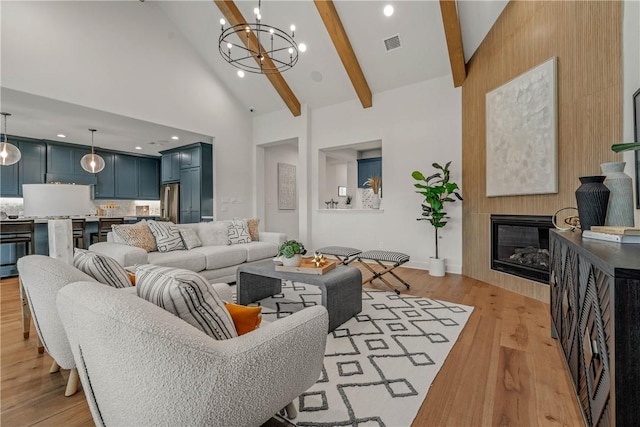 living room with light wood-type flooring, high vaulted ceiling, beamed ceiling, a fireplace, and a chandelier