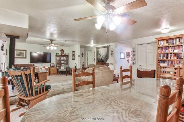 carpeted dining space with ceiling fan, a wood stove, and a textured ceiling