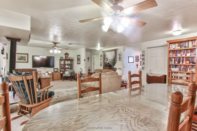 carpeted dining space with ceiling fan, a wood stove, and a textured ceiling