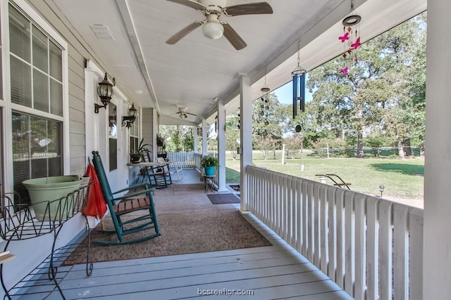 wooden terrace featuring a lawn, ceiling fan, and covered porch