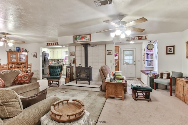 carpeted living room with a textured ceiling, a wood stove, and ceiling fan