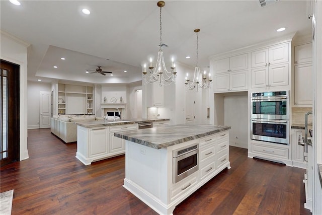 kitchen with white cabinets, a kitchen island, stainless steel appliances, and ceiling fan with notable chandelier