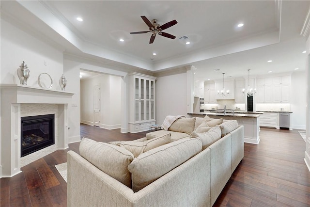 living room with a raised ceiling, a premium fireplace, ceiling fan, and dark wood-type flooring