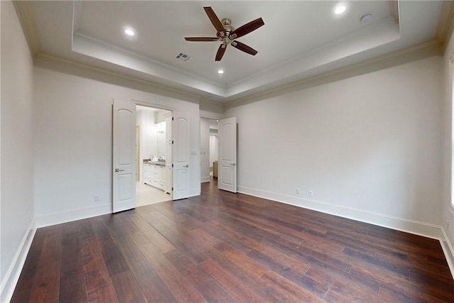 unfurnished bedroom featuring ensuite bathroom, ceiling fan, dark hardwood / wood-style floors, ornamental molding, and a tray ceiling