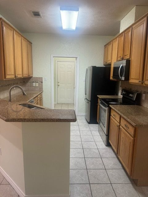 kitchen featuring backsplash, sink, light tile patterned floors, appliances with stainless steel finishes, and kitchen peninsula