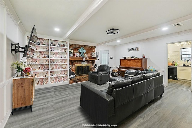 living room featuring an inviting chandelier, sink, a brick fireplace, beam ceiling, and wood-type flooring