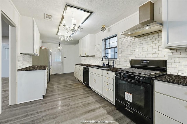 kitchen featuring white cabinetry, sink, hanging light fixtures, wall chimney range hood, and black appliances