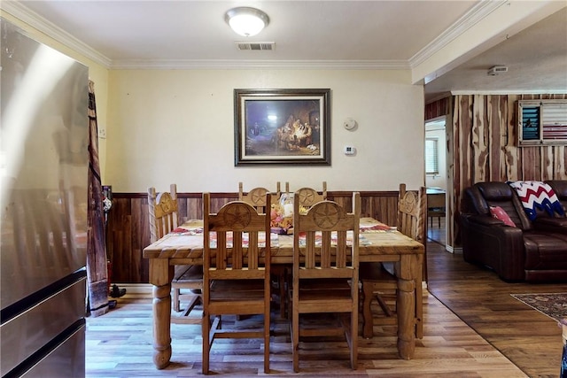 dining area featuring a wainscoted wall, visible vents, crown molding, and wood finished floors