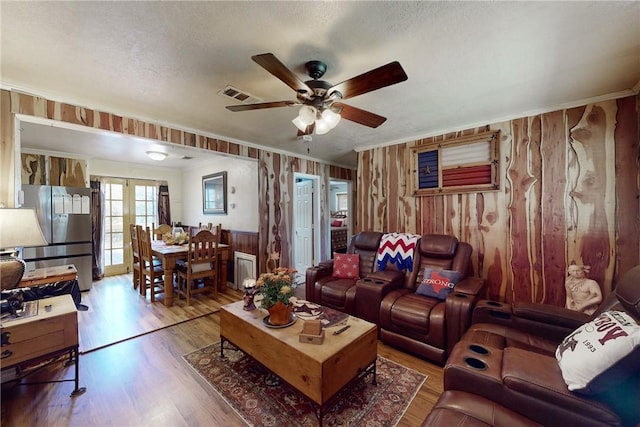 living room featuring ceiling fan, wood finished floors, visible vents, ornamental molding, and french doors