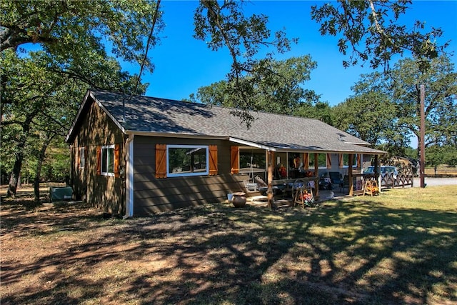 rear view of property with roof with shingles, a lawn, and a patio