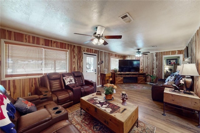 living area featuring visible vents, wood walls, a textured ceiling, and wood finished floors