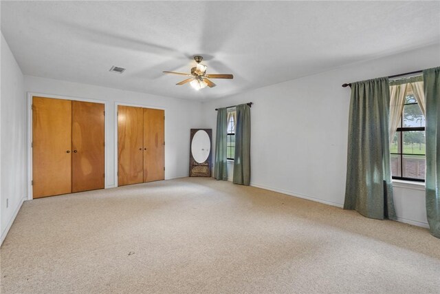 unfurnished bedroom featuring multiple closets, multiple windows, ceiling fan, and carpet