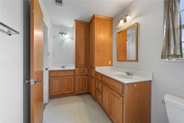 bathroom with toilet, a sink, visible vents, and double vanity