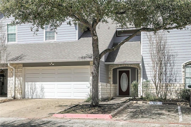 view of front of property featuring a garage, stone siding, and roof with shingles