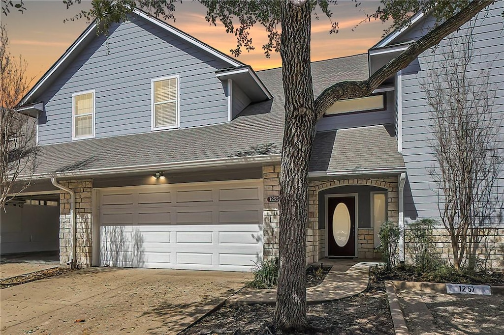 view of front of home featuring a garage, driveway, a shingled roof, and stone siding