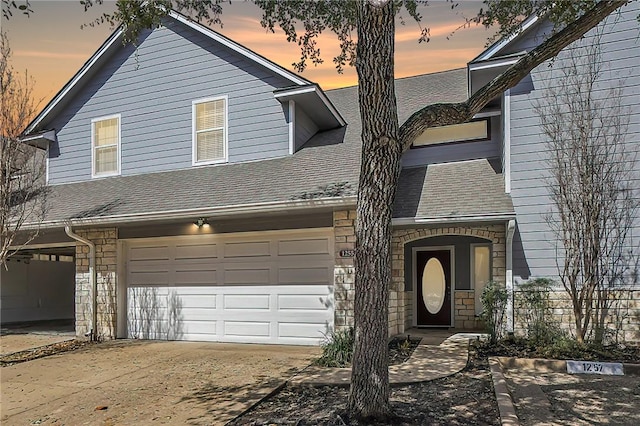 view of front of home featuring a garage, driveway, a shingled roof, and stone siding