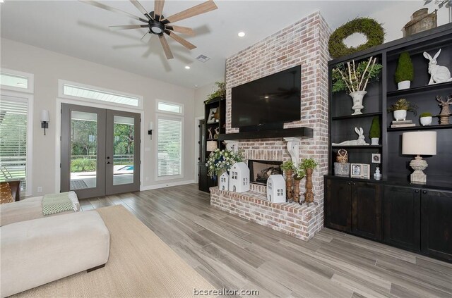 living room featuring ceiling fan, light wood-type flooring, a fireplace, and french doors