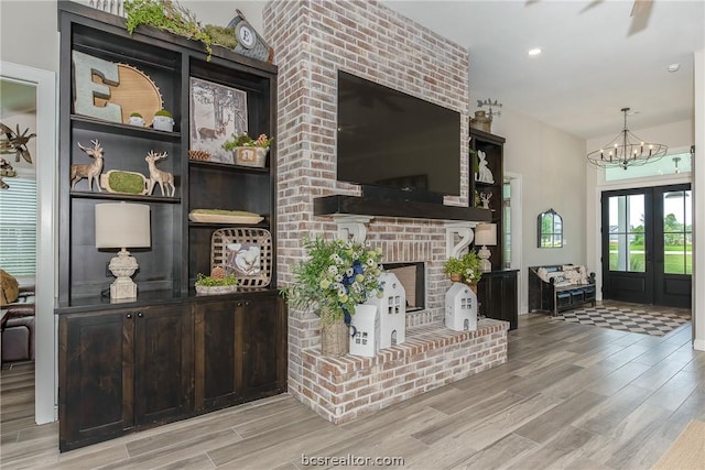 living room featuring a fireplace, french doors, light wood-type flooring, and a notable chandelier