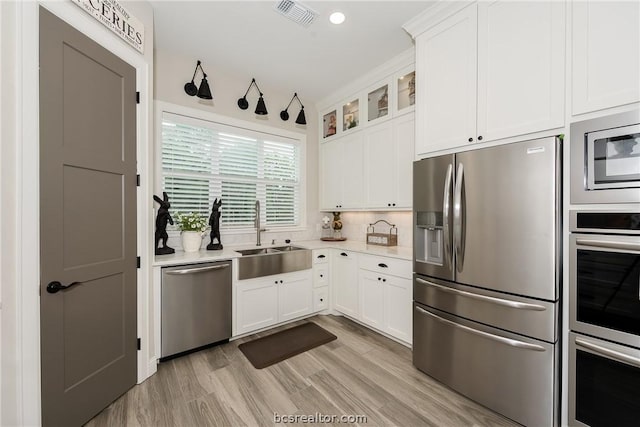 kitchen with sink, light hardwood / wood-style flooring, tasteful backsplash, white cabinetry, and stainless steel appliances