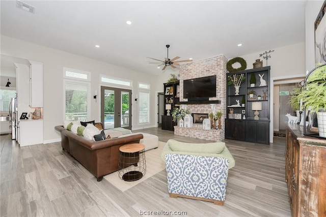 living room featuring french doors, light wood-type flooring, a brick fireplace, and ceiling fan