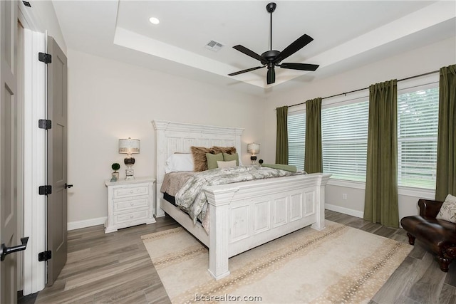 bedroom with a raised ceiling, ceiling fan, and hardwood / wood-style flooring