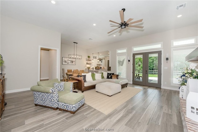 living room featuring french doors, ceiling fan with notable chandelier, and light hardwood / wood-style flooring