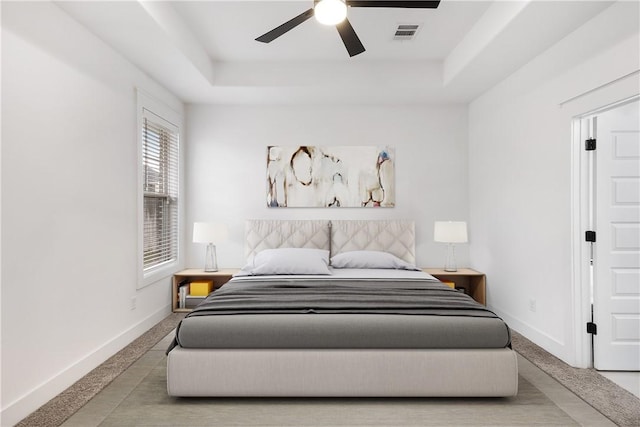 carpeted bedroom featuring baseboards, visible vents, a tray ceiling, and ceiling fan