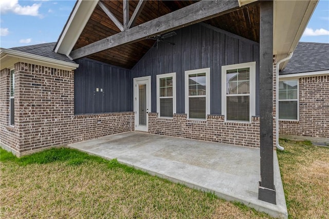 doorway to property featuring a yard, brick siding, a patio, and a shingled roof