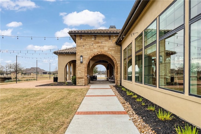 entrance to property featuring a tile roof, a chimney, stucco siding, a lawn, and stone siding