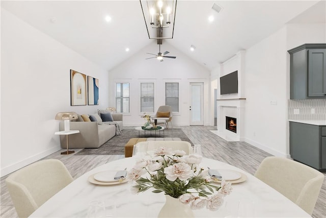 dining space with beam ceiling, visible vents, light wood-type flooring, a warm lit fireplace, and baseboards