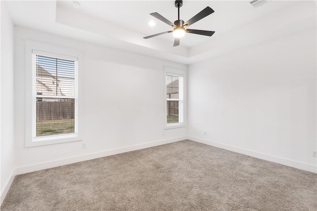 spare room featuring carpet, a raised ceiling, and baseboards