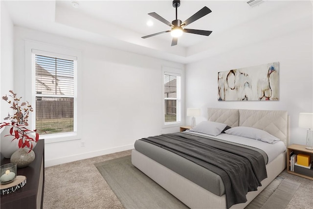 bedroom featuring a tray ceiling, light colored carpet, baseboards, and multiple windows