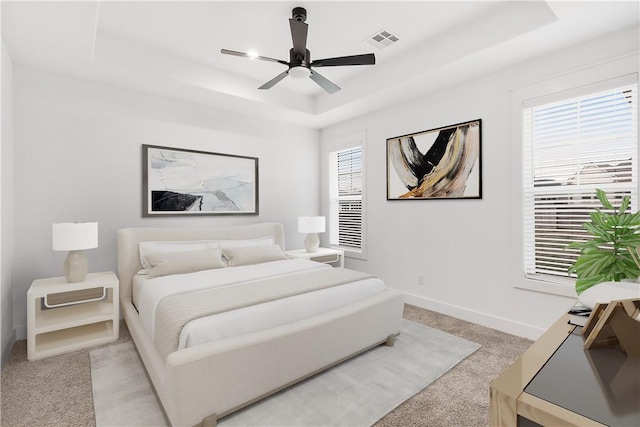 bedroom featuring light colored carpet, a raised ceiling, visible vents, and multiple windows