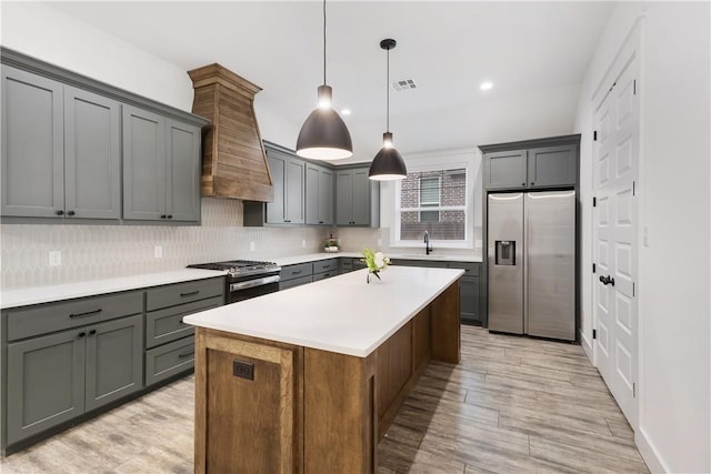 kitchen featuring light countertops, hanging light fixtures, appliances with stainless steel finishes, a kitchen island, and a sink