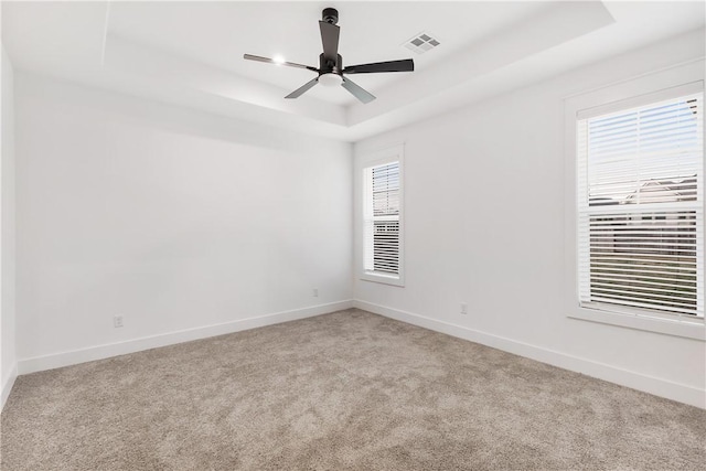 empty room featuring a raised ceiling, visible vents, baseboards, and a healthy amount of sunlight