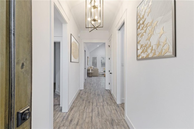 corridor with a chandelier, baseboards, and light wood finished floors