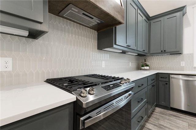 kitchen with gray cabinetry, stainless steel appliances, light countertops, and custom range hood