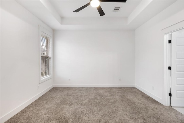 carpeted spare room featuring a tray ceiling, a ceiling fan, and baseboards