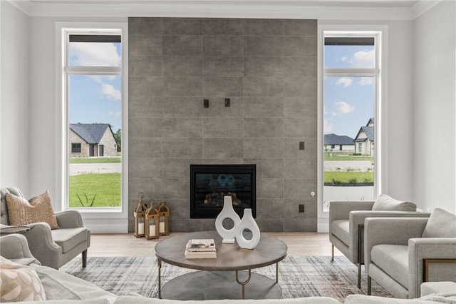 living room featuring plenty of natural light, wood-type flooring, ornamental molding, and a tiled fireplace