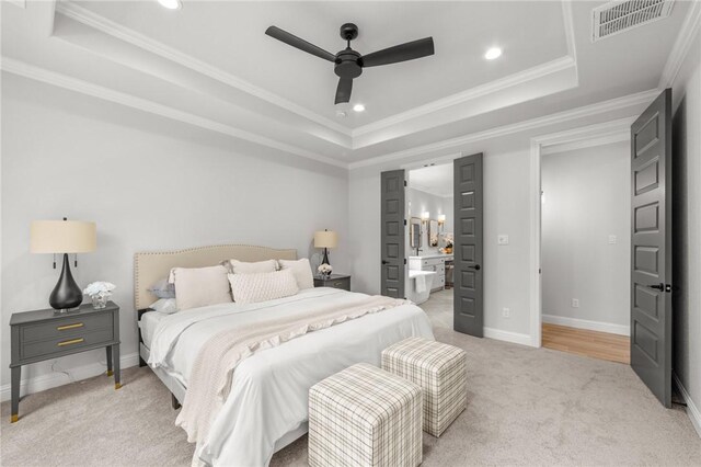 bedroom featuring connected bathroom, ceiling fan, a tray ceiling, light carpet, and ornamental molding